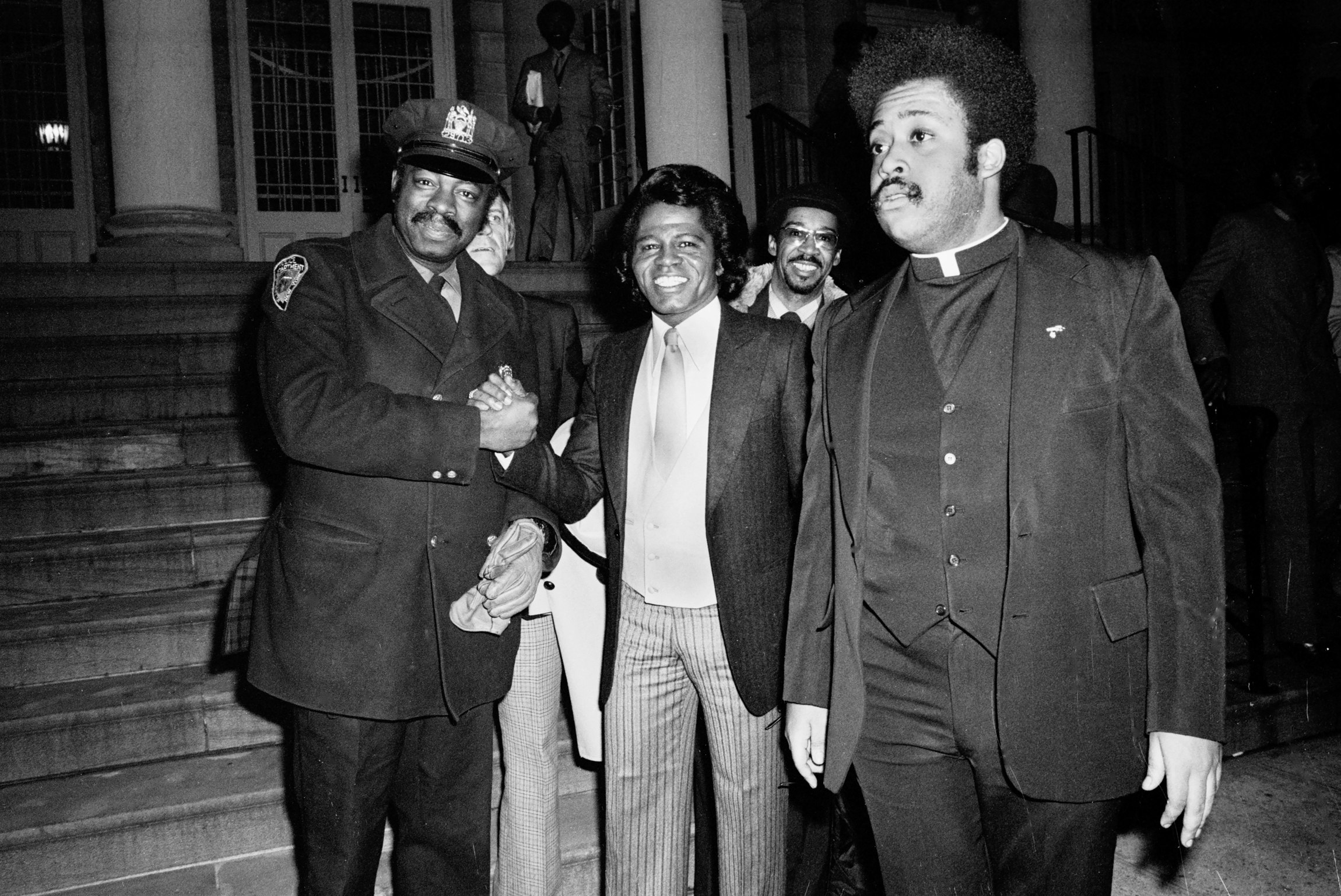 James Brown, with civil rights activist Reverend Al Sharpton by his side, shakes the hand of a New York City police officer outside City Hall, New York City, January 23, 1980. Photo by Gary Gershoff/Getty Images.